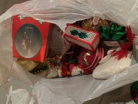 Plastic bag containing assorted Christmas decorations including a ceramic tree napkin holder, knitted items, and small ornaments.