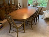Photo showing six wooden dining chairs placed around a large wooden dining table in a room with windows.