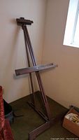 Full side view of the easel showing its tripod wooden structure and lower canvas shelf.