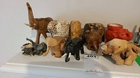 Overview of ten elephant figurines made from wood, ceramic and shell materials on white surface.