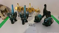 Photo of the entire lot showing two pairs of blue and dark green art glass elephant figurines, three gold metallic glass elephants on glass bases, and dark ceramic elephants.