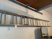 View of the entire aluminum extension ladder laid horizontally against wall showing length and structure.