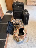 Photo showing all five luggage items including floral duffel bag, black backpack, carry-on suitcase, laptop bag, and a larger suitcase on a carpeted floor.