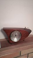 Side view of the full clock showing Mid-Century Modern styled wooden case, brass legs, and attached electric cord.