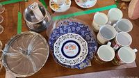 Overhead view of assorted serving platters, blue and white lattice souvenir plate, floral ceramic tea cups, and ceramic mugs.