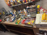 Overview of wooden workbench with various tools and hardware including drill bits, hand tools, spray cans, and metal organizer