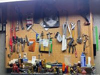 Full view of pegboard with various hand tools including scrapers, screwdrivers, sockets, pliers, saw blades, a flashlight, and replacement bits hung and placed on shelf below