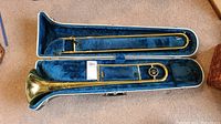 Trombone fully seated inside an open blue plush lined hard case, showing the full length of the trombone and its components.