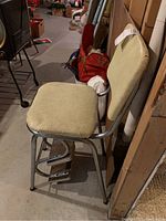 Side view of vintage heavy upholstered metal stool with footrests in basement with visible wear and dirt.