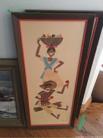 Framed ethnic style painting with two figures carrying fruit, signed by the artist, wood frame with orange trim