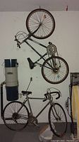 Two bicycles hung on wall in garage; one blue mountain bike with straight handlebars and one silver Schwinn men's racing bike with drop handlebars.