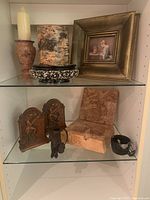 Full view of shelf with candle holders, vase, framed print, carved wooden box, carved panels, figurine and bowl