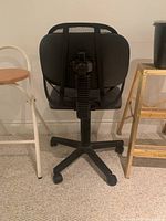 Back view of black mesh office desk chair on rolling wheels without armrests