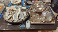 Mixed flatware such as spoons, spreaders along with glass salt and pepper shakers, bowls, syrup dispenser, and trays arranged on two trays.