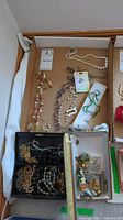 Overview of assorted necklaces, brooches, pins, and earrings laid out in cardboard tray.