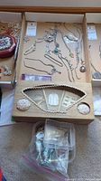 Top view of assorted necklaces, bracelets, wrist clocks, and brooches displayed in a cardboard box. Includes chains, pendants, and decorative wrist clocks.