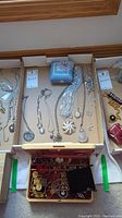 View of jewelry laid out in cardboard tray including silver-tone necklaces, bracelets, trinket box and small container with jewelry.