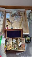 Full view of assorted jewelry including necklaces, bracelets, brooches, pins, and coin pouches arranged in a box with a wooden jewelry box in foreground.