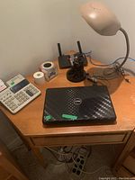 Dell laptop closed on wooden desk with TI 5045 II adding machine, desk lamp, and some cables and small office items