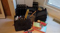 Photo showing black plastic vertical file organizers, a black briefcase, some stationery boxes, and rulers scattered on carpeted floor near window.