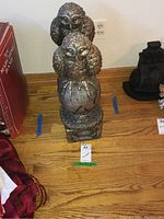 Two owl statues on a wooden surface with an electrical outlet in the background, showing front and side views.