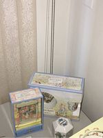 Image of boxed Peter Rabbit Wedgwood plate and mug set along with Ginger and Pickles music box and piggy bank on table against white wall.