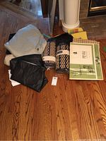 Overview of assorted placemats and linens on wooden floor including rolled placemats, folded textiles, and a sealed package of dinner mats.
