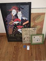 The full set of four framed prints arranged standing on hardwood floor, showing large 'The Mikado' print and three smaller framed artworks or documents.