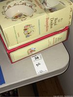 Two boxed sets of Royal Doulton Bunnykins tableware displayed stacked on a small table, showing packaging with Bunnykins branding and illustrations of the items inside.