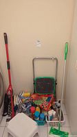 Photo showing red Swiffer mop, green folding step stool, white Rubbermaid step stool, various cleaning cloths and basket with cleaning products.