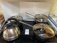 Front view of stainless steel tea kettle and three hard-anodized cookware pieces on stovetop