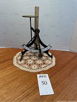 Front angle view of an antique iron and brass letter scale on a lace doily with a ruler next to it showing its height.
