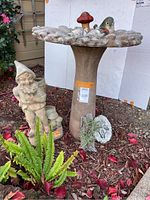 Full view of bird bath, gnome statue and surrounding decorative accessories in outdoor garden setting.