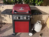 Full front view of Brinkmann gas BBQ grill showing red hood and black base with two knobs, side burner, propane tank, and wheels