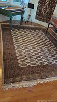 Full view of the entire rug laid out on a hardwood floor in a room, showing the overall design, border, and fringe.