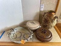 Four pottery items arranged on a flat surface: large glazed bowl with spiral handles, two lidded serving vessels, and a decorated jug with handles.