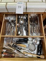 Full drawer view showing flatware sections with forks, spoons, knives, and below assorted kitchen utensils and knives.