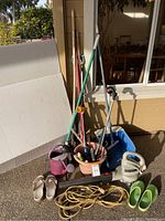 Photo showing the full lot including Craftsman electric blower, garden tools, watering cans, and garden shoes arranged outdoors near a house wall and sliding door.