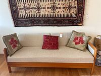 Front view of sofa with three throw pillows and textile wall hanging