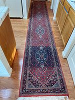 Full view of the long runner in a kitchen hallway showing the red, black, and blue geometric floral pattern extending over its length on hardwood floor.