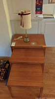 Three teak-colored nested tables stacked with the smallest in front. Tabletops show signs of wear.