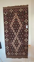 Full front view of the patterned rug showing diamond and cross motifs in earth tones and fringed edges.
