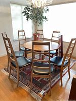 Seven wood ladder-back chairs around round teak table on rug beneath chandelier