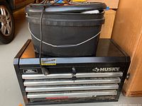 Black Husky 4-drawer top tool chest with black plastic bucket on top and power cord draped