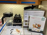 Vitamix Professional Series 750 blender base with control panel, 64-oz container with lid, tamper, original box, recipe book, and manuals displayed on countertop