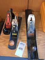 Three manual hand planes on wooden surface: red-painted Craftsman plane, black Buck Bros plane and Stanley plane
