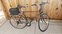 Side view of the full bicycle showing the entire black frame, tires, seat, handlebars, rear rack with bag, and pedals.