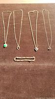 Group shot of four necklaces and one bracelet laid on dark fabric.