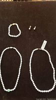 Lot laid out on black surface showing two pearl necklaces, a pearl bracelet, and a pair of pearl earrings.