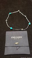 Full view of braided silver chain with turquoise and decorative silver beads laid out around John Hardy pouch